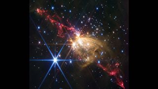 Streaks of red gas mix with young stars in the darkness of space as two large jets spew out on either side of a glowing yellow center, creating a magnificent nebula