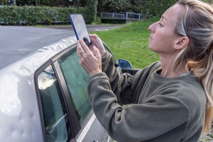 Female taking picture of her damaged car after an hailstorm.