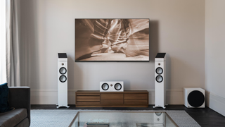 A lifestyle shot showing a white set of Monitor Audio Bronze 7G Series speakers in a brightly lit, neutral colored room underneath a large TV