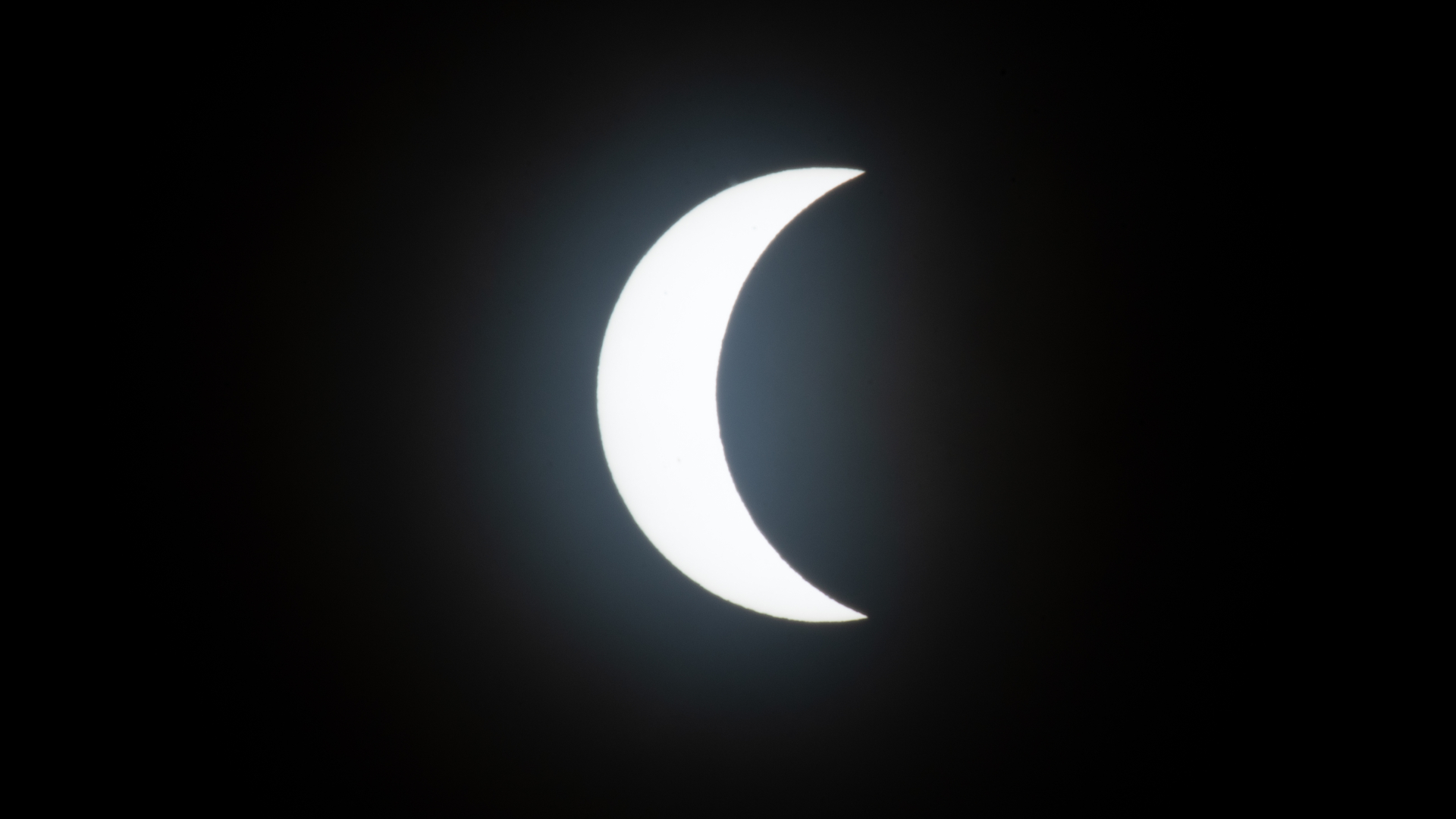 The sun appears as a glowing crescent in a black sky with the moon partially eclipsing its surface
