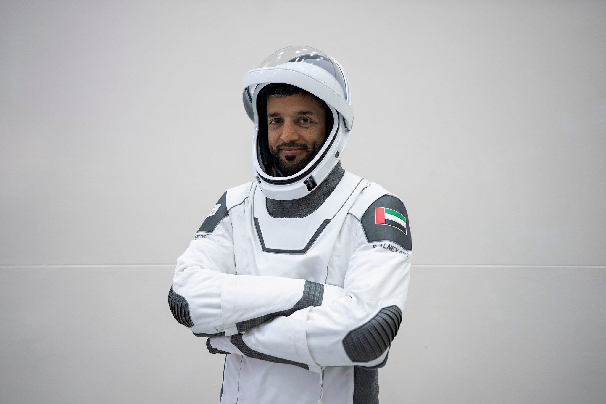 sultan al-neyadi stands in a spacesuit with arms folded