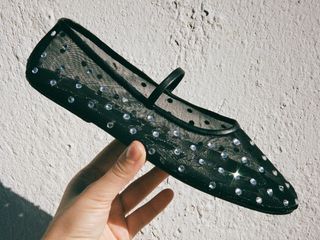 An image cropped to someone's hand holding a Jeffrey Campbell mesh ballet flat with rhinestones