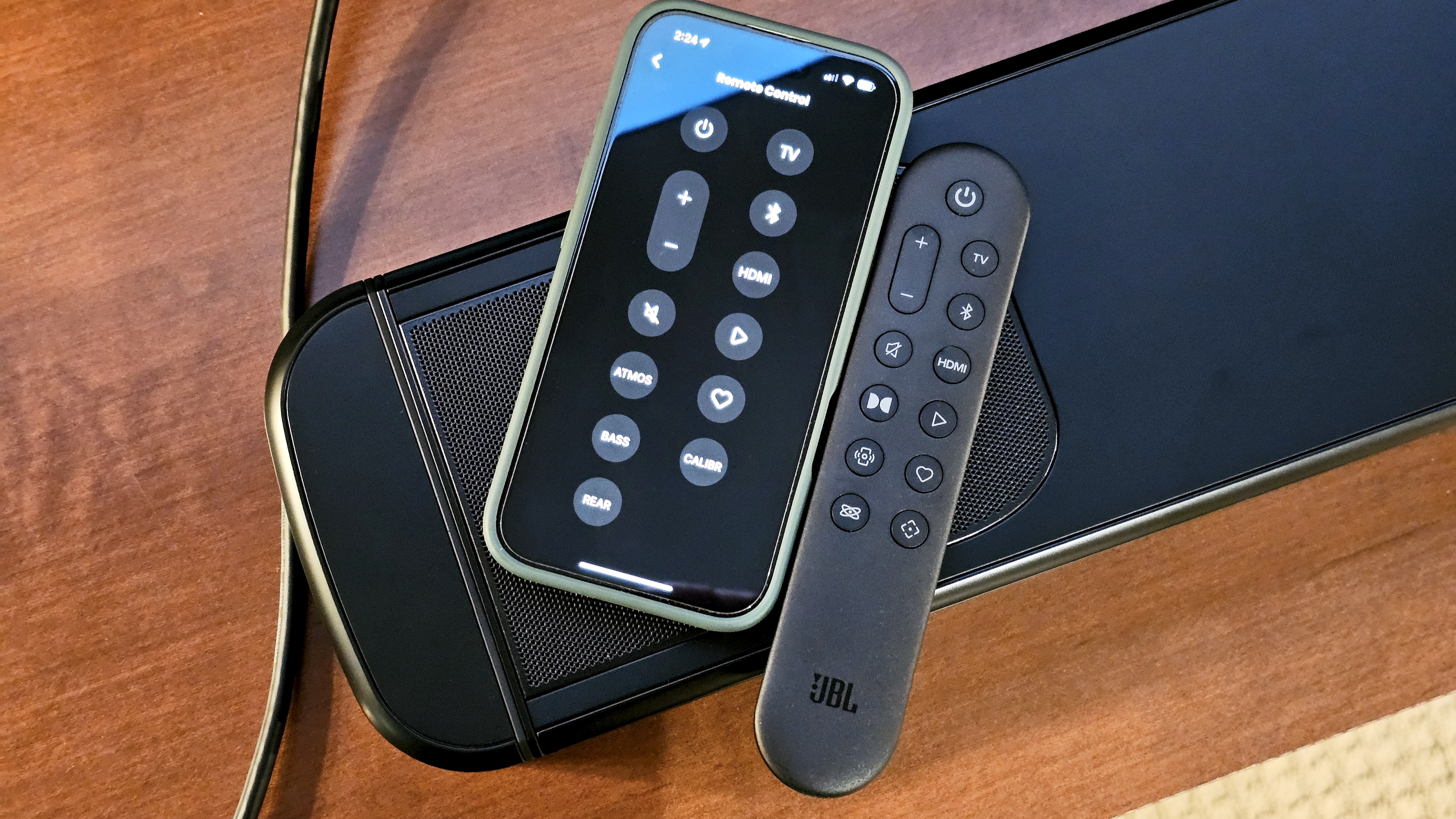 JBL Bar 1000MK2 on TV stand with remote control and phone running JBL One app