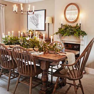 a dining room with a wooden dining table a and spindle back dining chairs set for Christmas dinner with candles on the table and in an overhead chandelier