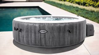 An Intex PureSpa Greywood Deluxe Inflatable Hot Tub Set - 6 Person next to a pool