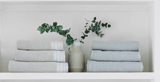 Bathroom shelf with folded towels next to a vase with eucalyptus