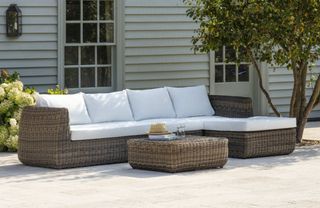 A dark brown rattan chaise garden sofa with white cushions
