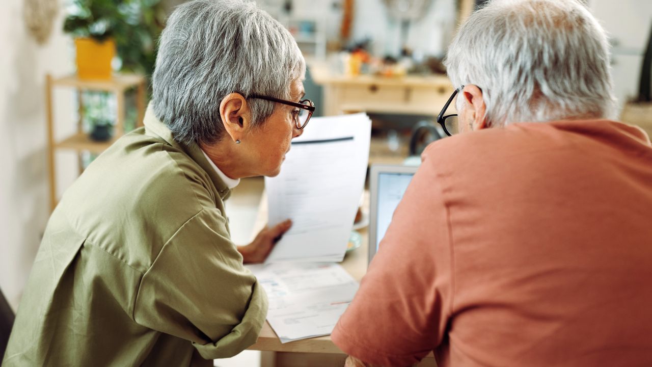 An older couple go over financial paperwork at a table and with a laptop. 