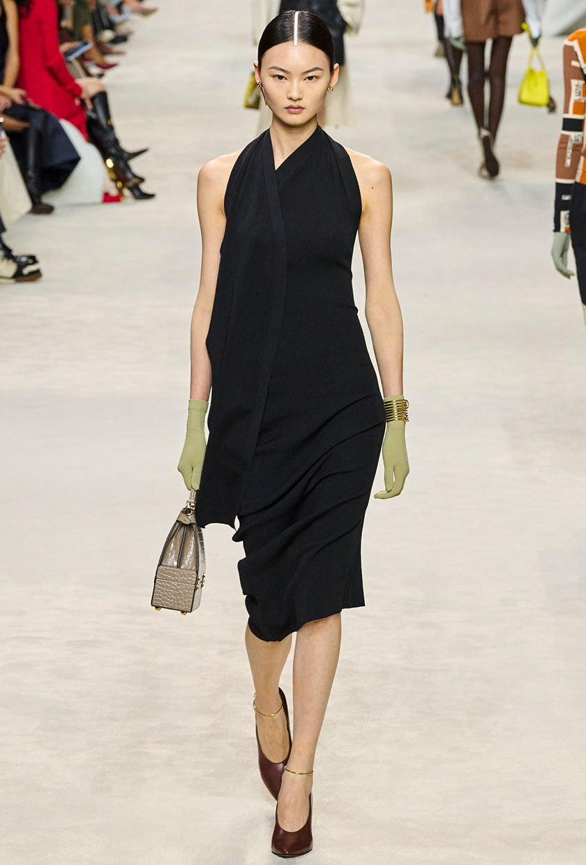 halter dress trend on the Fendi Spring 2024 runway with a model wearing a black midi knit dress styled with pistachio green gloves, brown pointed pumps, and a tan bag