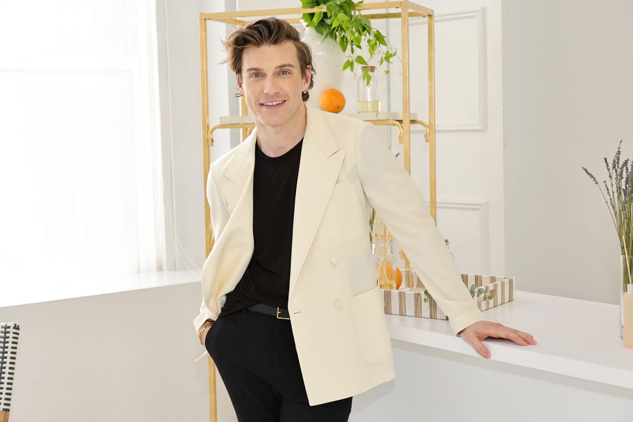 A picture of a man leaning on a white table and smiling at the camera