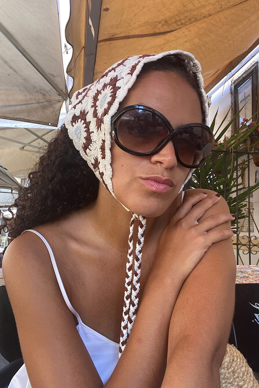 how to pack for Italy is shown in a photo of a fashion editor wearing a crochet scarf, brown sunglasses, and a white dress