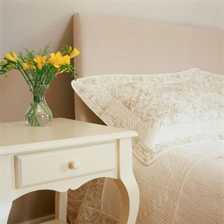 white bedside table with flowers next to neutral pillow