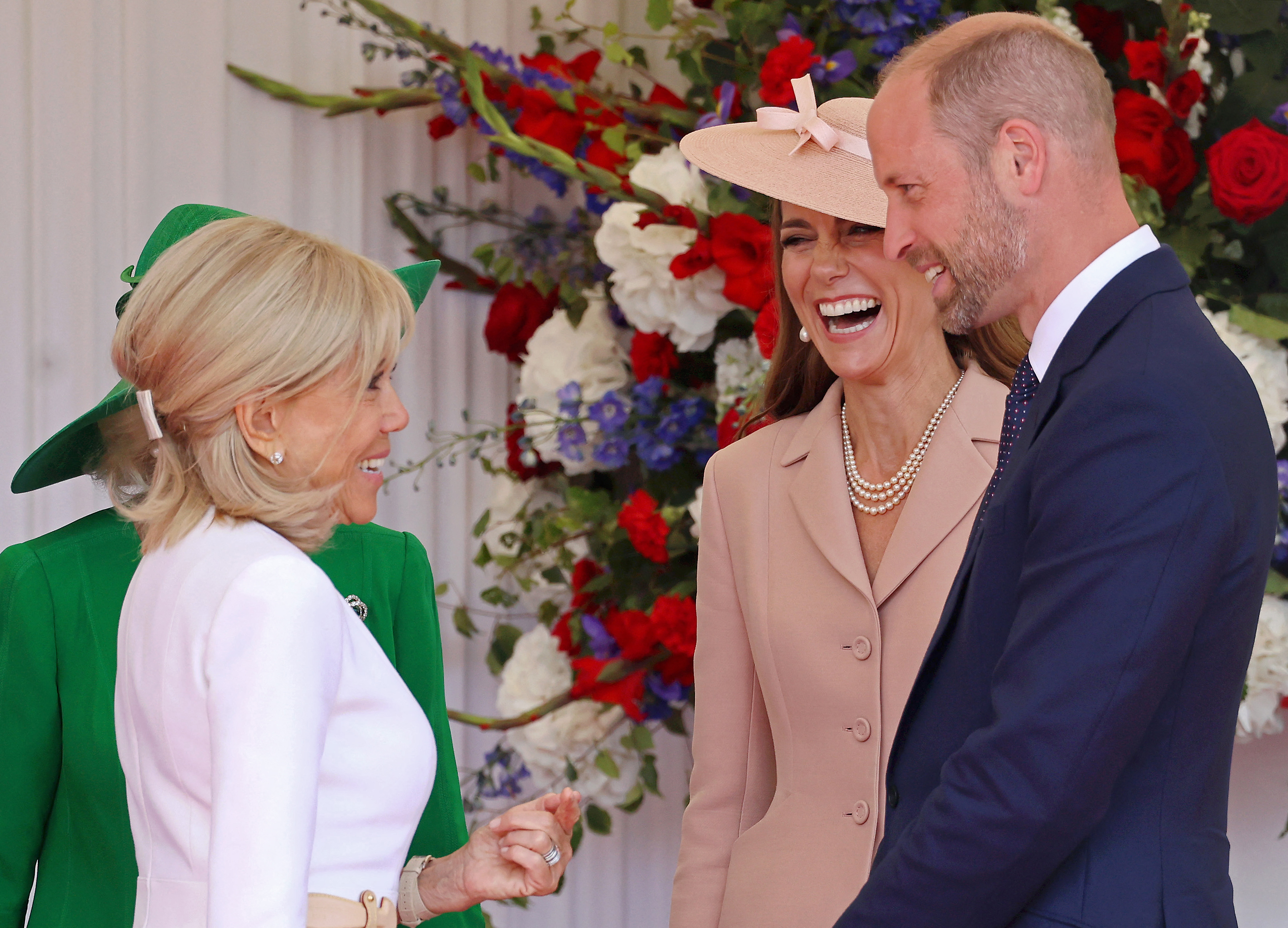 Kate Middleton, Brigitte Macron and Prince William talking and laughing in front of red, white and blue flowers