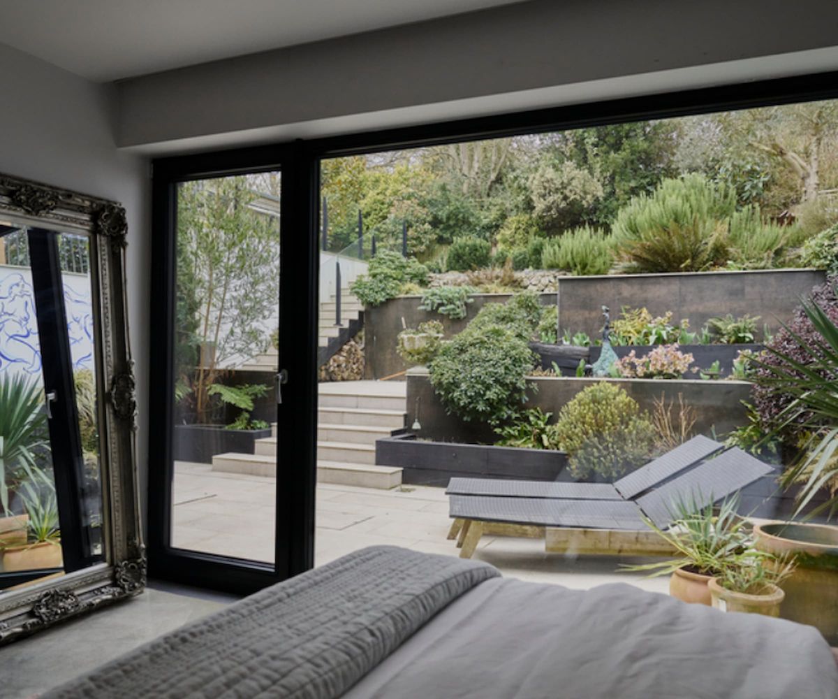 A bedroom with large picture windows looking out onto a tiered garden
