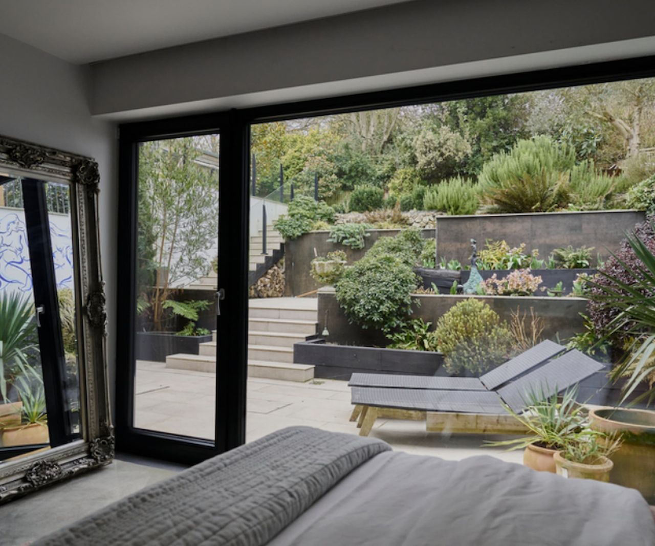 A bedroom with large picture windows looking out onto a tiered garden