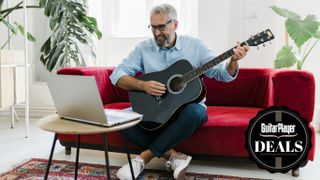 Man in blue shirt plays black acoustic guitar on a red couch