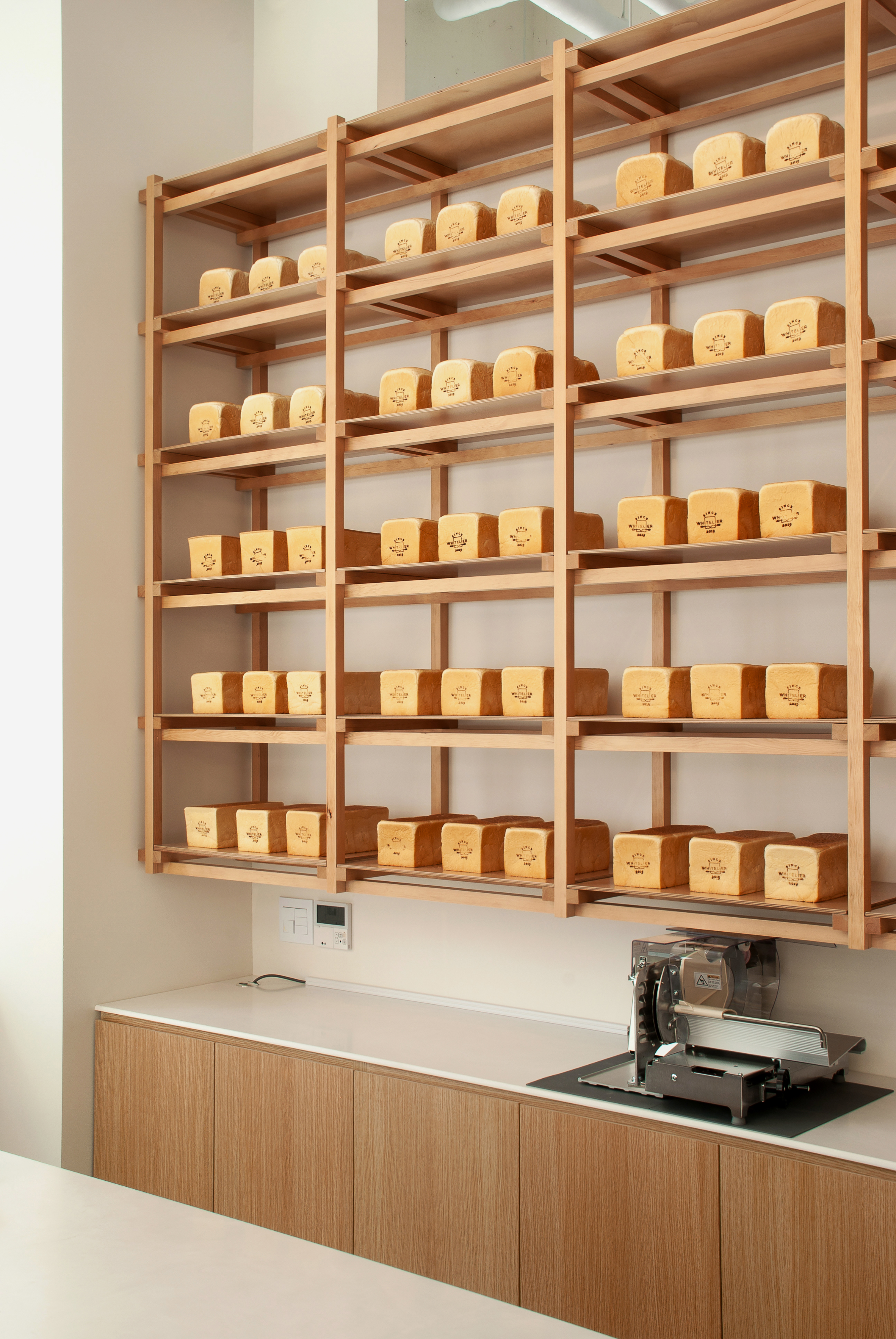 Loaves of bread on shelving with bread slicer on counter below