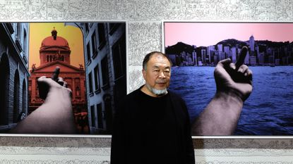 Ai Weiwei poses with paintings from his "Who Am I?" art exhibition