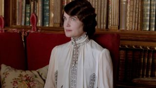 Elizabeth McGovern sits with a patient smile in the library in Downton Abbey.