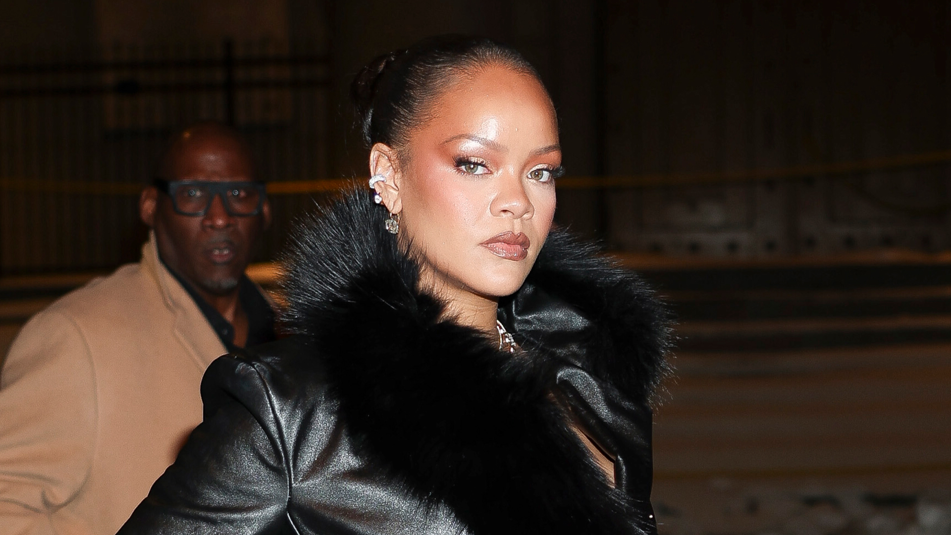 Rihanna is seen on February 13, 2026 in New York City wearing a fur-trimmed leather trench coat, lace underwear, sheer tights, and pointed-toe pumps