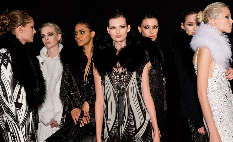 Seven female models wearing black and white pieces from Roberto Cavalli&#039;s collection. Some pieces are patterned, some are sleeveless and some feature fur. The background is black