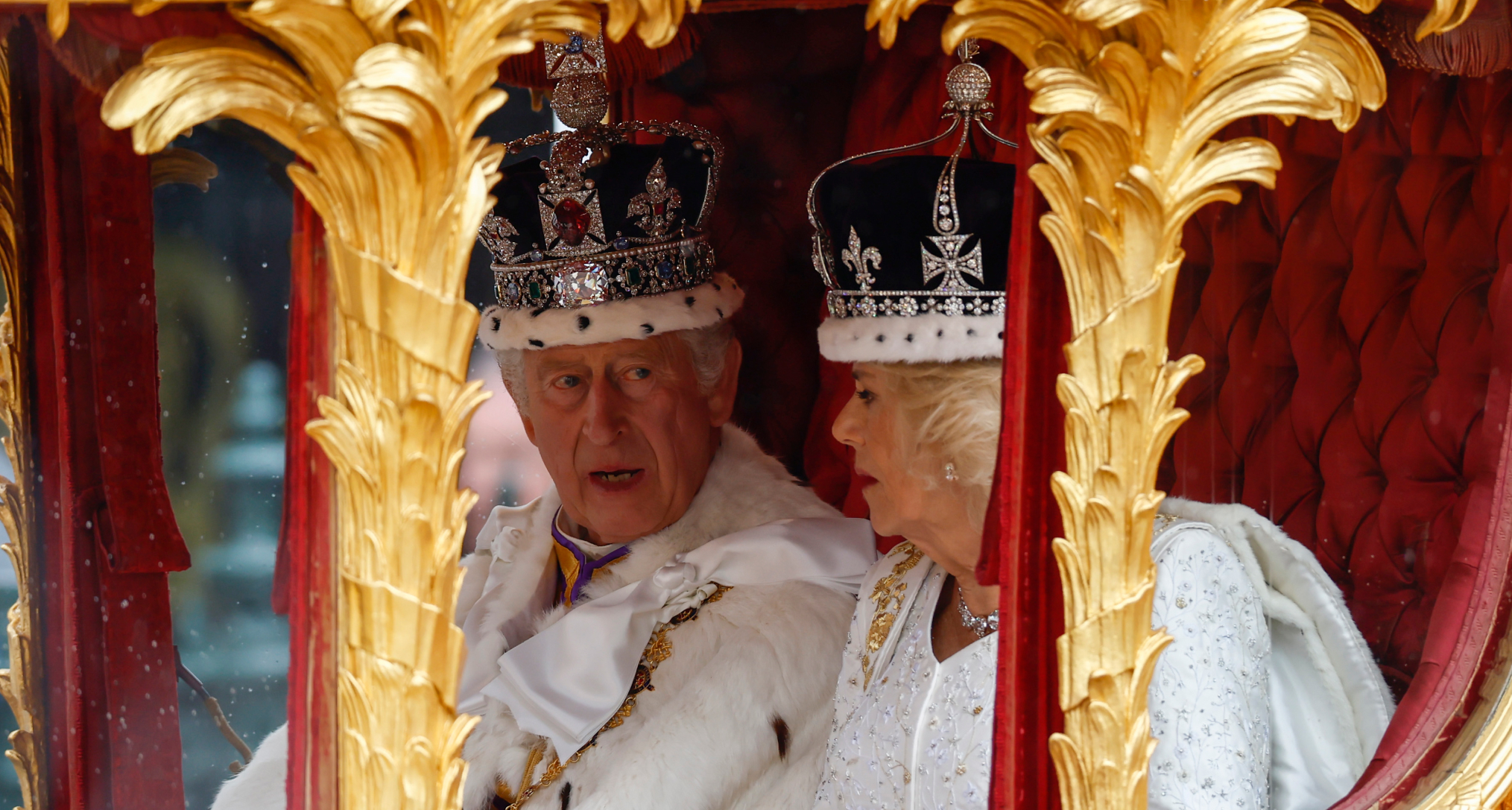 Queen Camilla and King Charles riding in a gold carriage wearing crowns