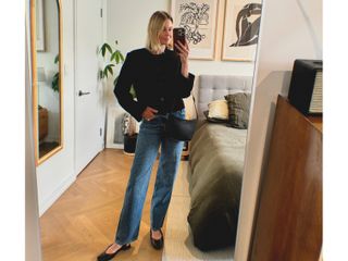 Natalie Cantell takes a mirror selfie in her apartment in New York, wearing a classic outfit: Reformation Val jeans, a Harris Tapper cropped black collarless blazer, flat black J. Crew sling-back shoes, and carrying a black Celine Croque bag.