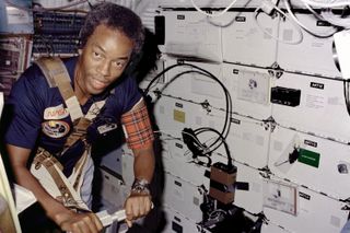 On Challenger's middeck, mission specialist GuionBluford, restrained by harness and wearing blood pressure cuff on his left arm, exercises on the treadmill.