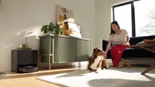 Roomba j9+ in its base station in a bright living room with a person playing with their dog