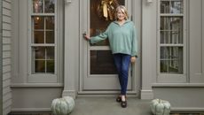 martha stewart opening the door to her home with a fall wreath and pumpkins on the steps