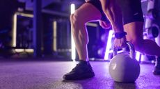 A gym athlete lifting a kettle bell off the floor, bathed in purple light