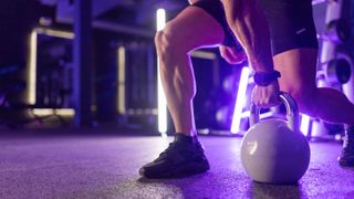 A gym athlete lifting a kettle bell off the floor, bathed in purple light