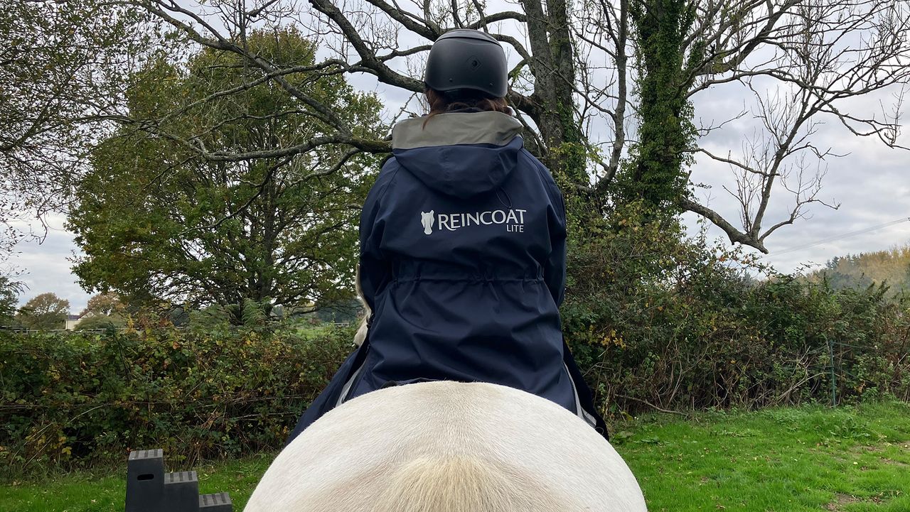 Rider wears Reincoat Lite on horse, viewed from the back