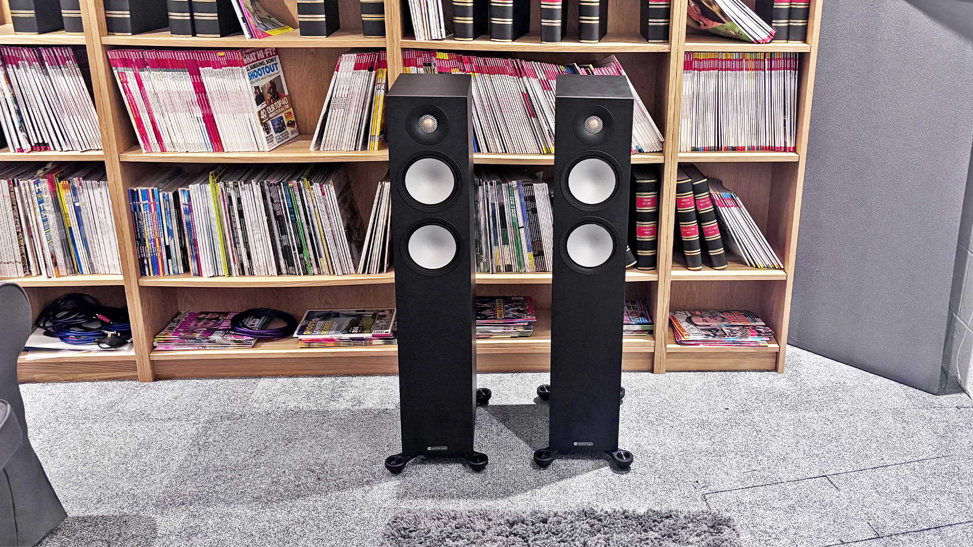 Monitor Audio Bronze 300 7G floorstanding speakers on grey carpet in front of bookcase