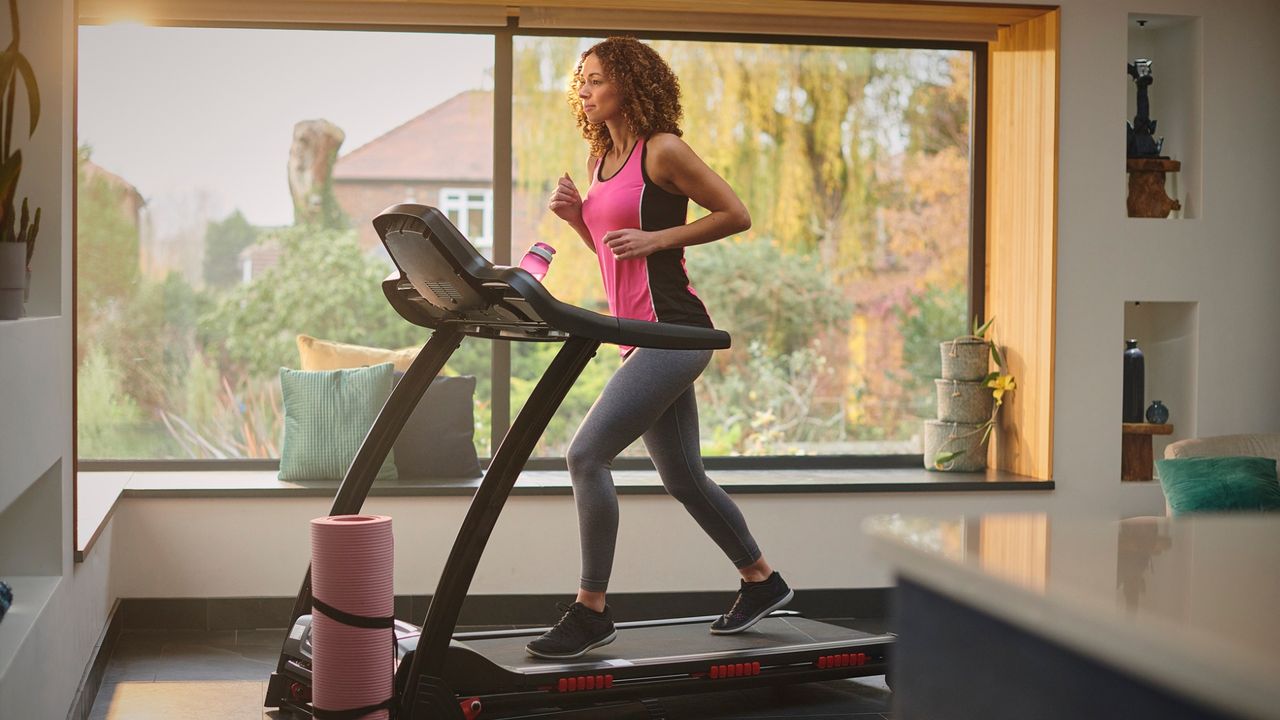 woman on a treadmill in a home setting with a large window behind her