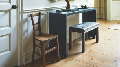 A cozy entryway in a colonial-style home, featuring low-slung a mid-century style chair, bench, and console table topped with various objects