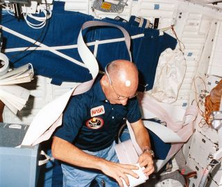 STS-8 mission specialist Bill Thornton working with a roll of teletype paper aboard the space shuttle Challenger in 1983.