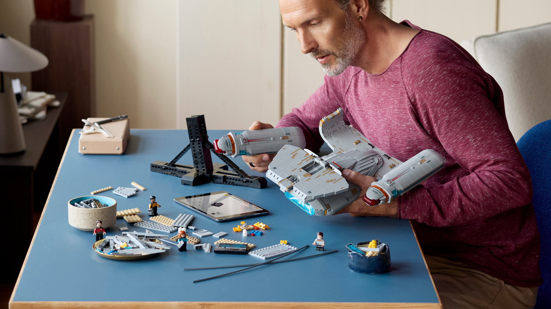 A man constructs the Lego Enterprise set while sat at a blue table