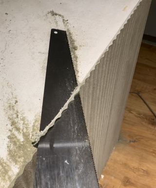 Cutting fluted panel with a hand saw, picture shot from above to show horizontal placement of saw to trim top edge of fluted panel at 90 degrees to the ground