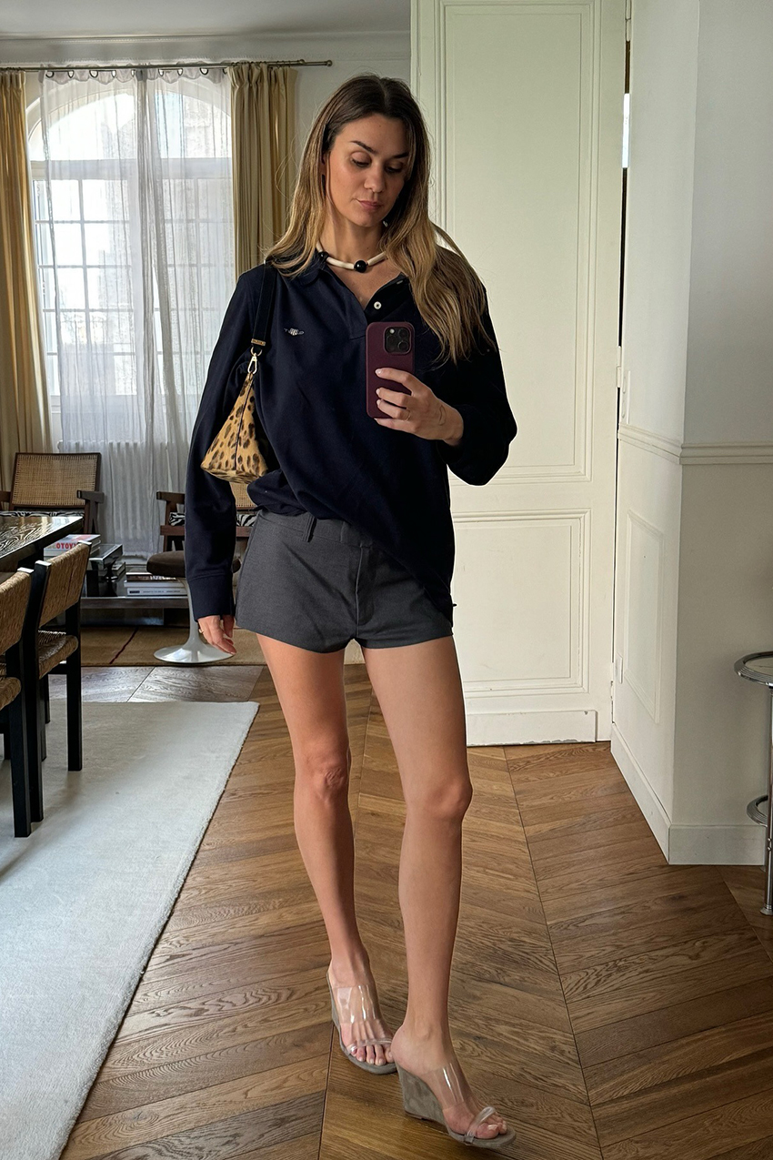 a woman wearing a black polo shirt, gray shorts, clear wedge sandals, and animal print bag