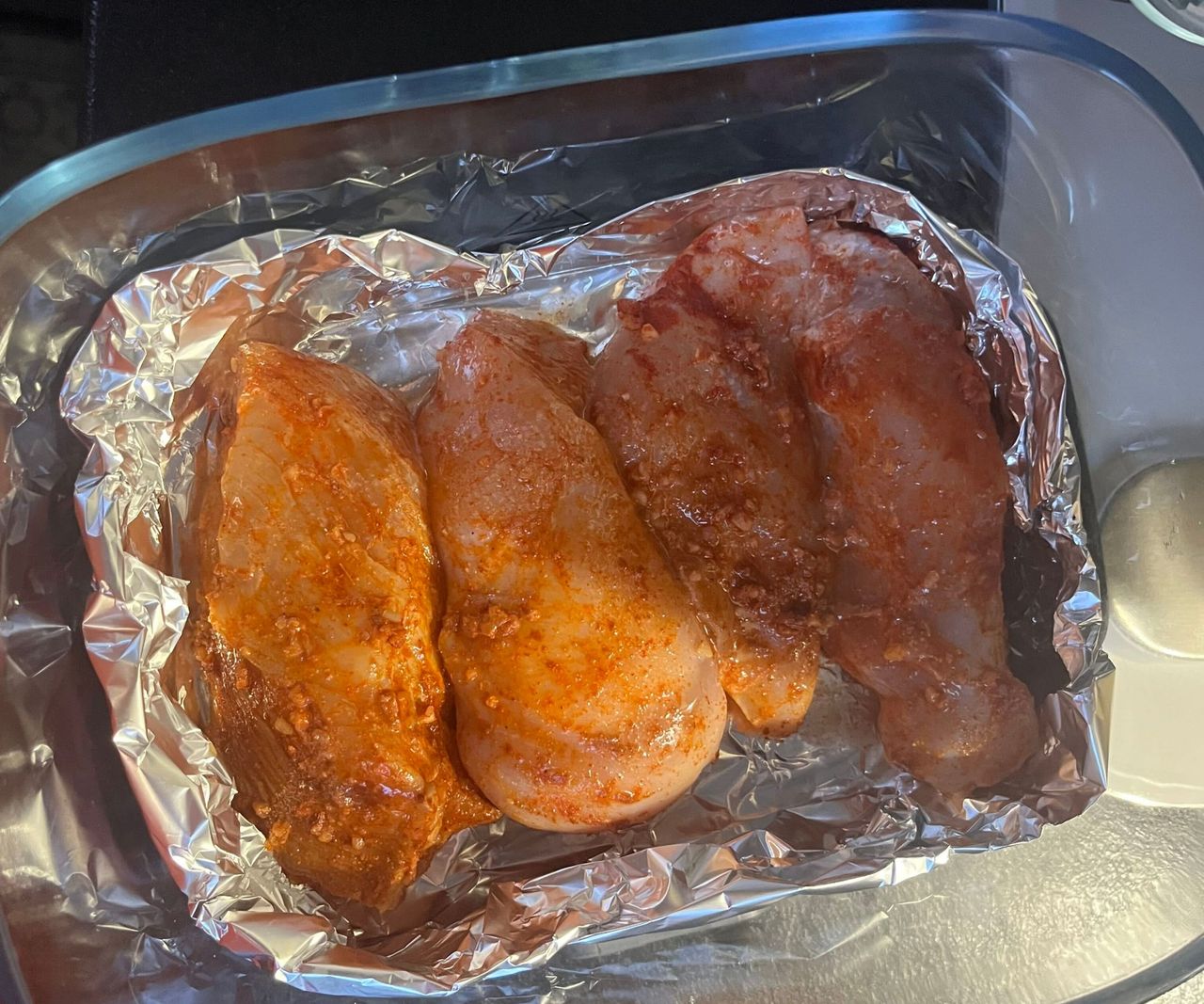 Four raw seasoned chicken breasts in foil in a glass air fryer basket