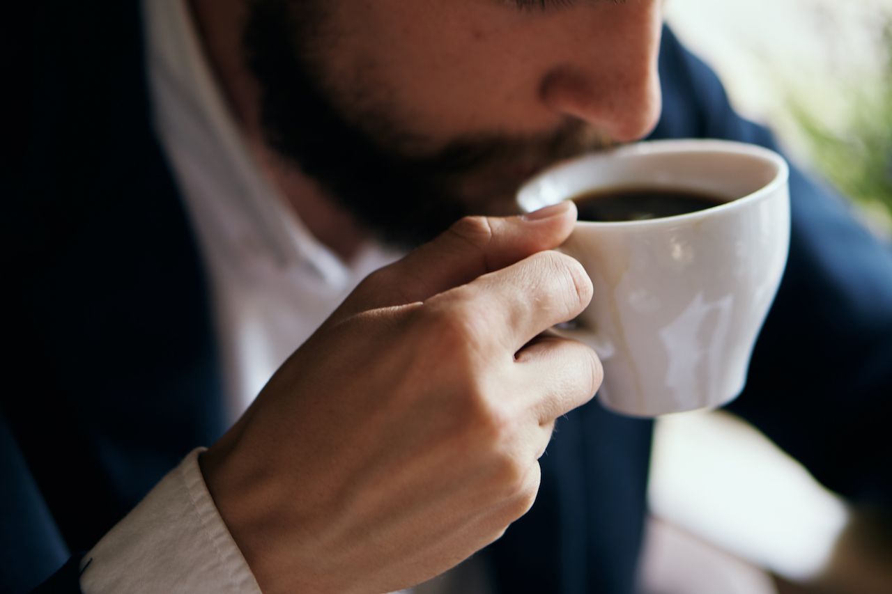 close up of a man wearing a suit and taking a sip of coffee from a mug