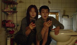 Parasite Ki-jeong and Ki-woo check their phones in the bathroom