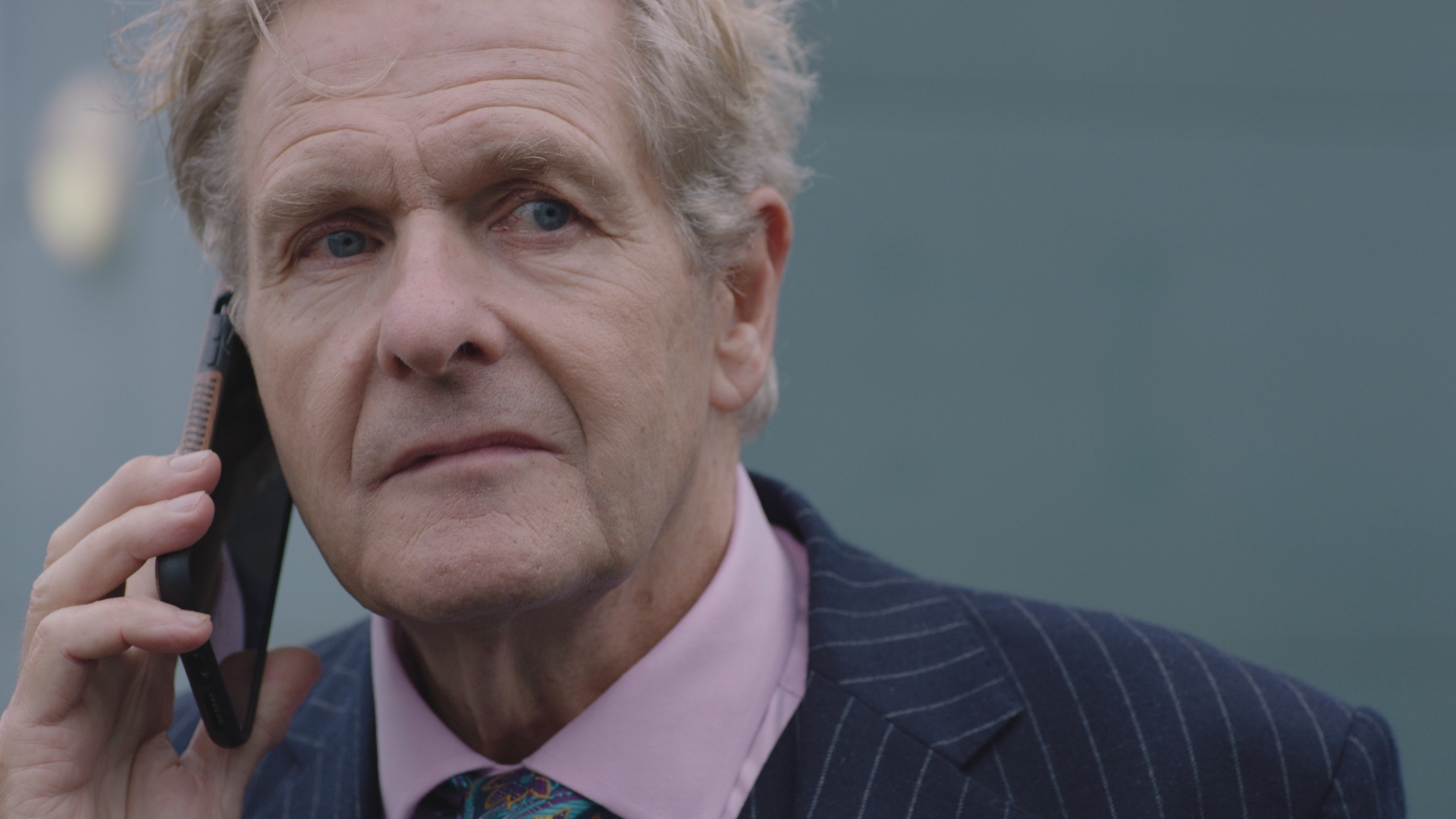 Russell wearing a pinstriped suit and on his mobile phone outside the hospital.