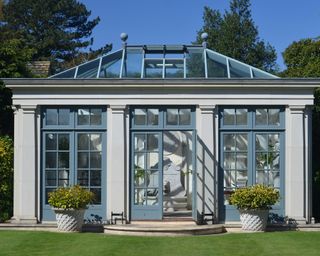 impressive grey and blue orangery by Haddonstone, with large grey planters either side of the blue doors