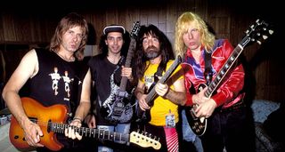 1991, a historic moment for electric guitar as Joe Satriani [pictured in a ball cap] jammed onstage with Spinal Tap, who are pictured here with Nigel Tufnel on the far left with a T-style, Derek Smalls in a yellow T-shirt with a headless bass, while a pouting David St. Hubbins cradles a Les Paul.