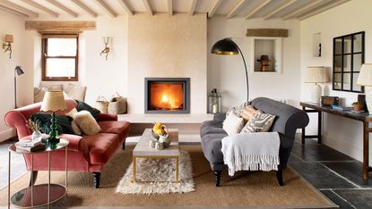 living room with modern fire lit and grey and pink sofas in room with white walls and painted beams