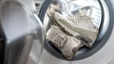 A pair of white sneakers being put into a washing machine