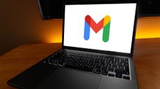 Gmail logo symbol pictured on a laptop screen placed on top of a desk with warm orange lighting in background.