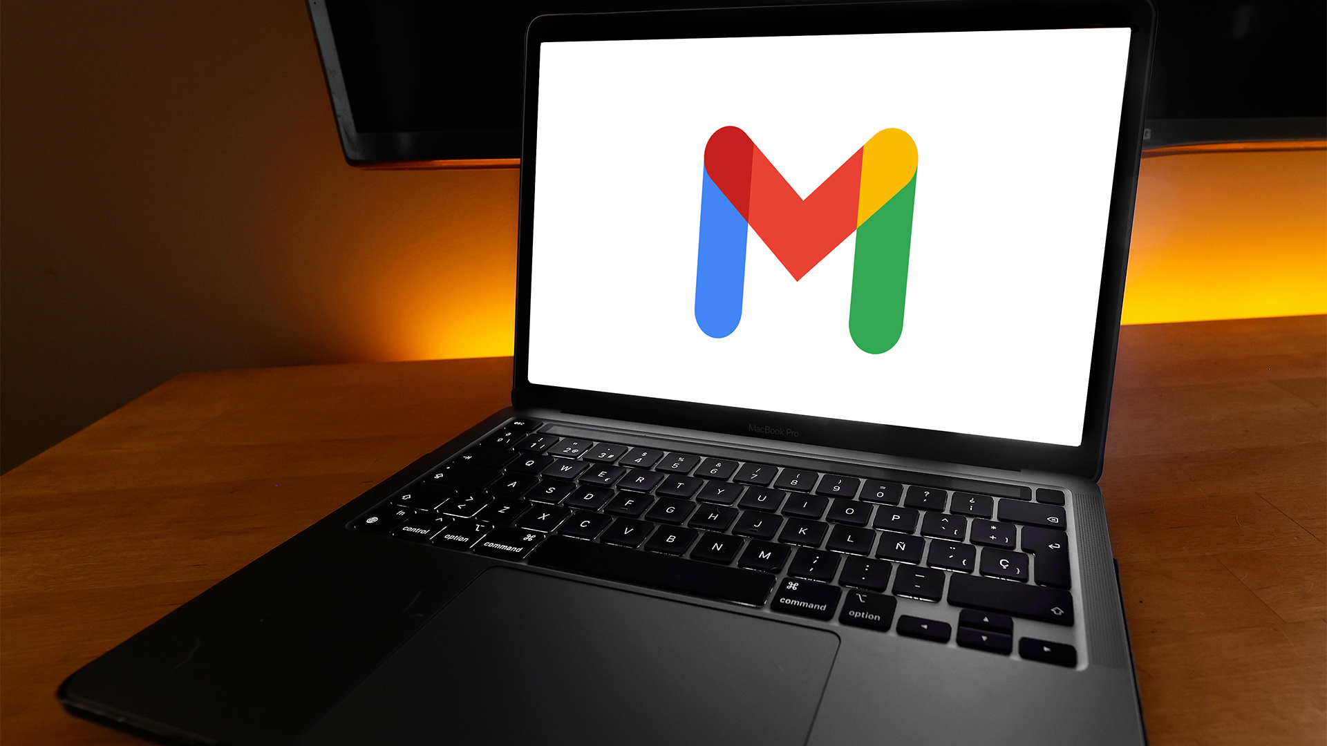 Gmail logo symbol pictured on a laptop screen placed on top of a desk with warm orange lighting in background.